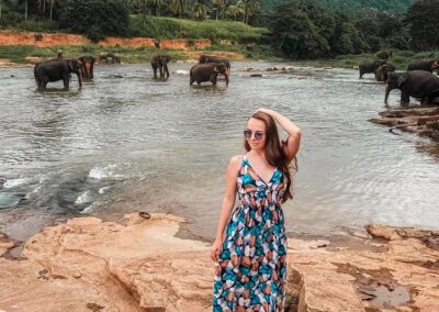 A young foreign girl standing on a rocky terrain by the river, at Pinnawala Elephant Orphanage.