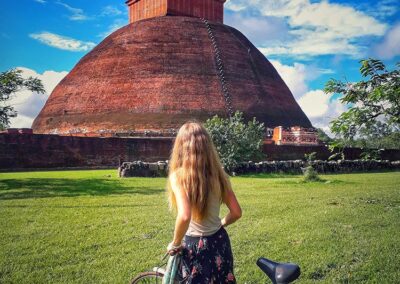 A foreigner, standing with a bicycle, in front of a large brick stupa, while exploring the Ancient City of Anuradhapura