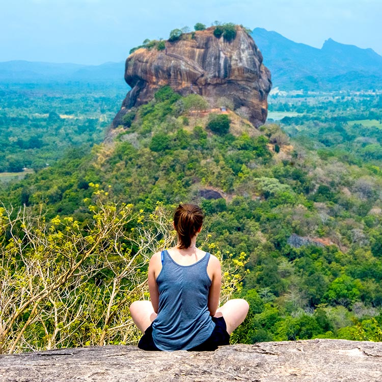 A foreign lady sitting on the Pidurangala rock top, witnessing the view of the Sigiriya Rock Fortress