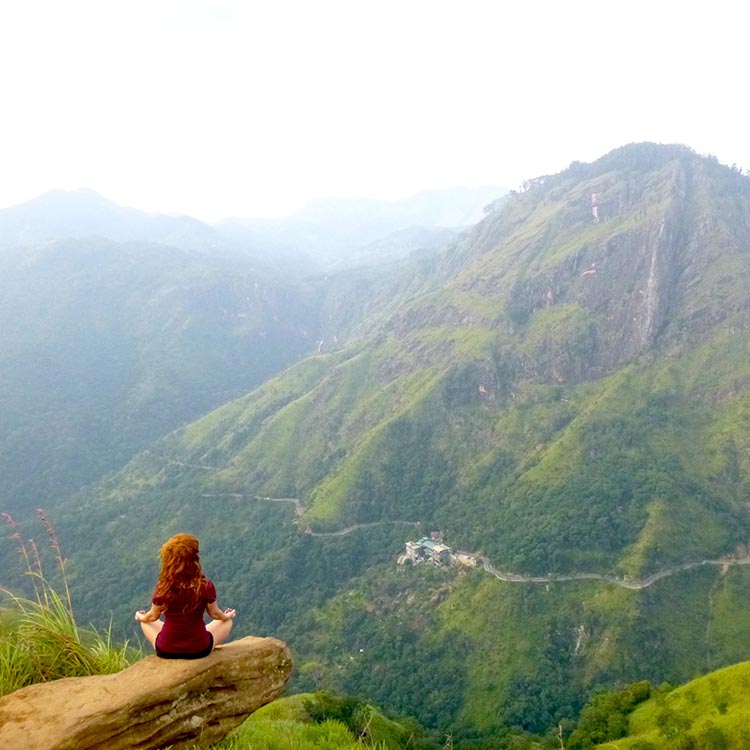 A foreign girl sitting on the top of the rock in the meditating pose