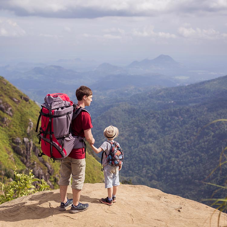 A father and a son with two backpacks at a top of a mountain while hiking