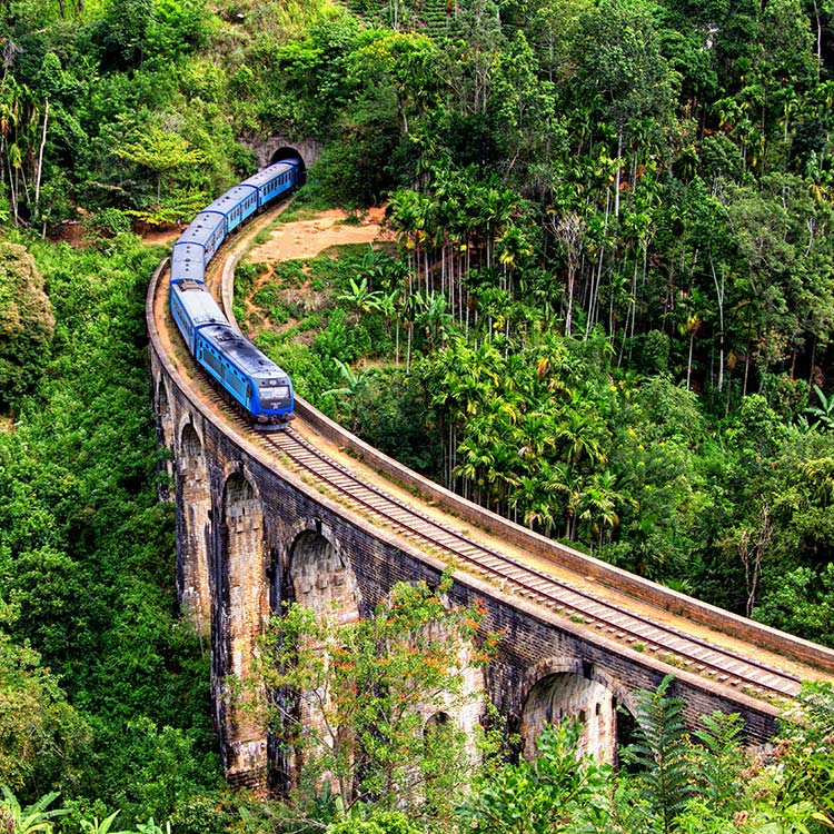A blue train riding over the Massive Nine Arch Bridge in Ella, Sri Lanka that stands amidst the greenery