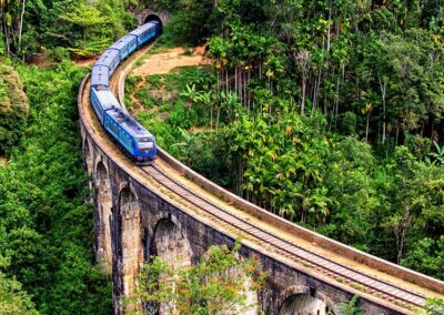 A Blue colour train passing over the Nine Arch Bridge that stands amidst a verdant surrounding.