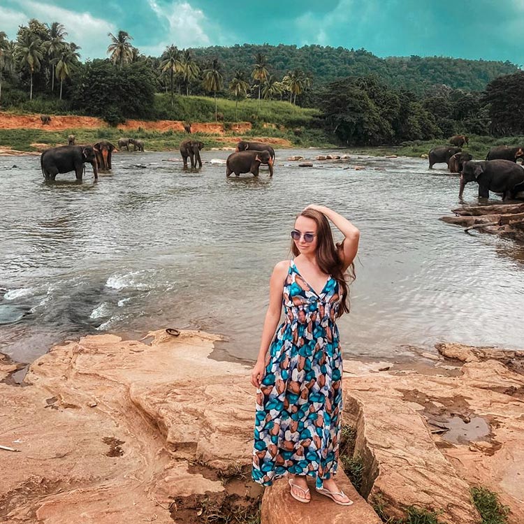 A young foreign girl standing on a rocky terrain by the river, at Pinnawala Elephant Orphanage.