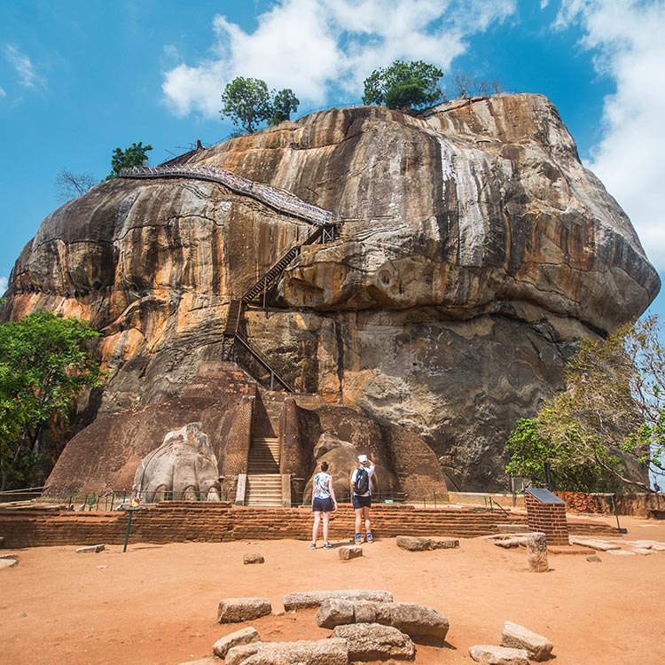 Two foreigners standing in front of the gigantic Sigiriya Rock Fortress that stands with Majesty