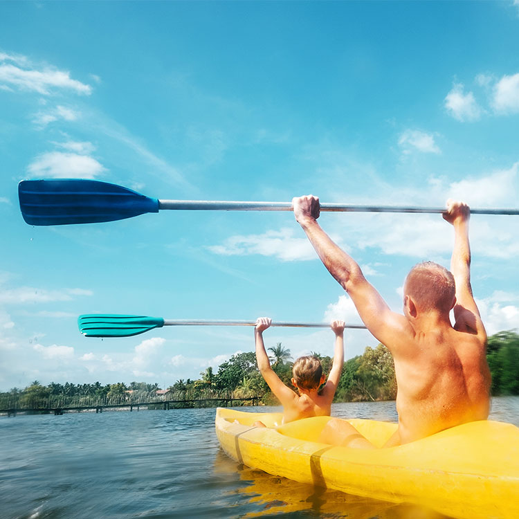 A Father and Son with their hands held high with their paddles while Enjoying Kayaking