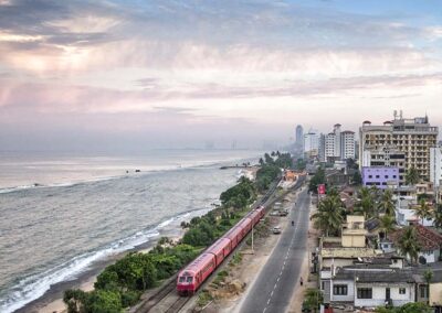 A train traveling on a railway line, the ocean, shore, and the buildings of the City of Colombo
