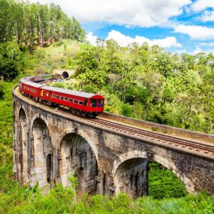 A red train traveling over the Nine Arches Bridge