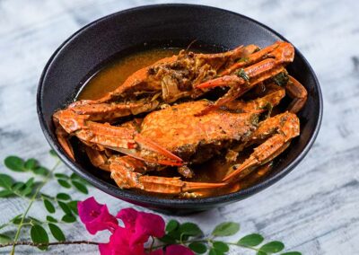 A dish of the brown Jaffna Crab Curry with a flower next it
